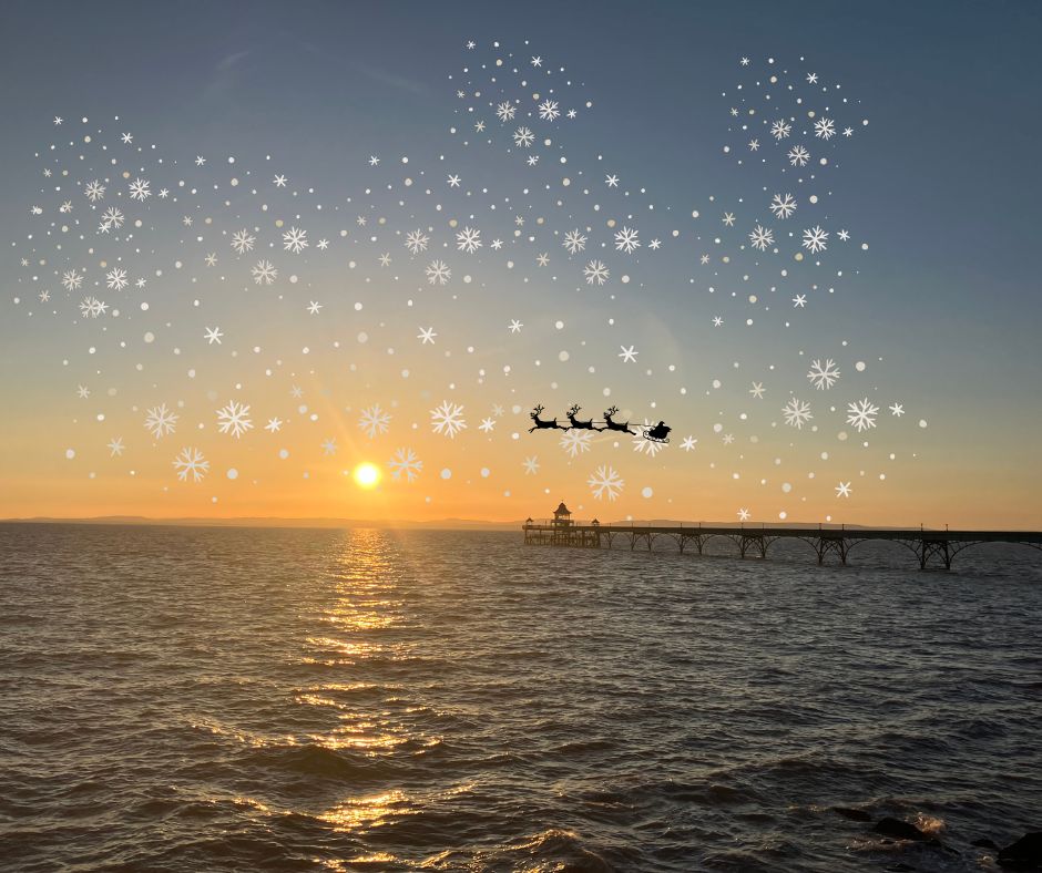 Christmas Clevedon Pier photographed at sunset with snowflakes and a silhouetted Santa riding a sleigh pulled by reindeer.